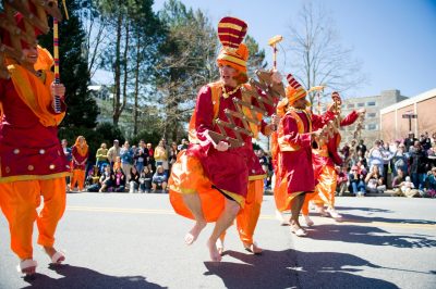 Dancers in bright orange costumes perform in front of a large crowd at the street fair. 