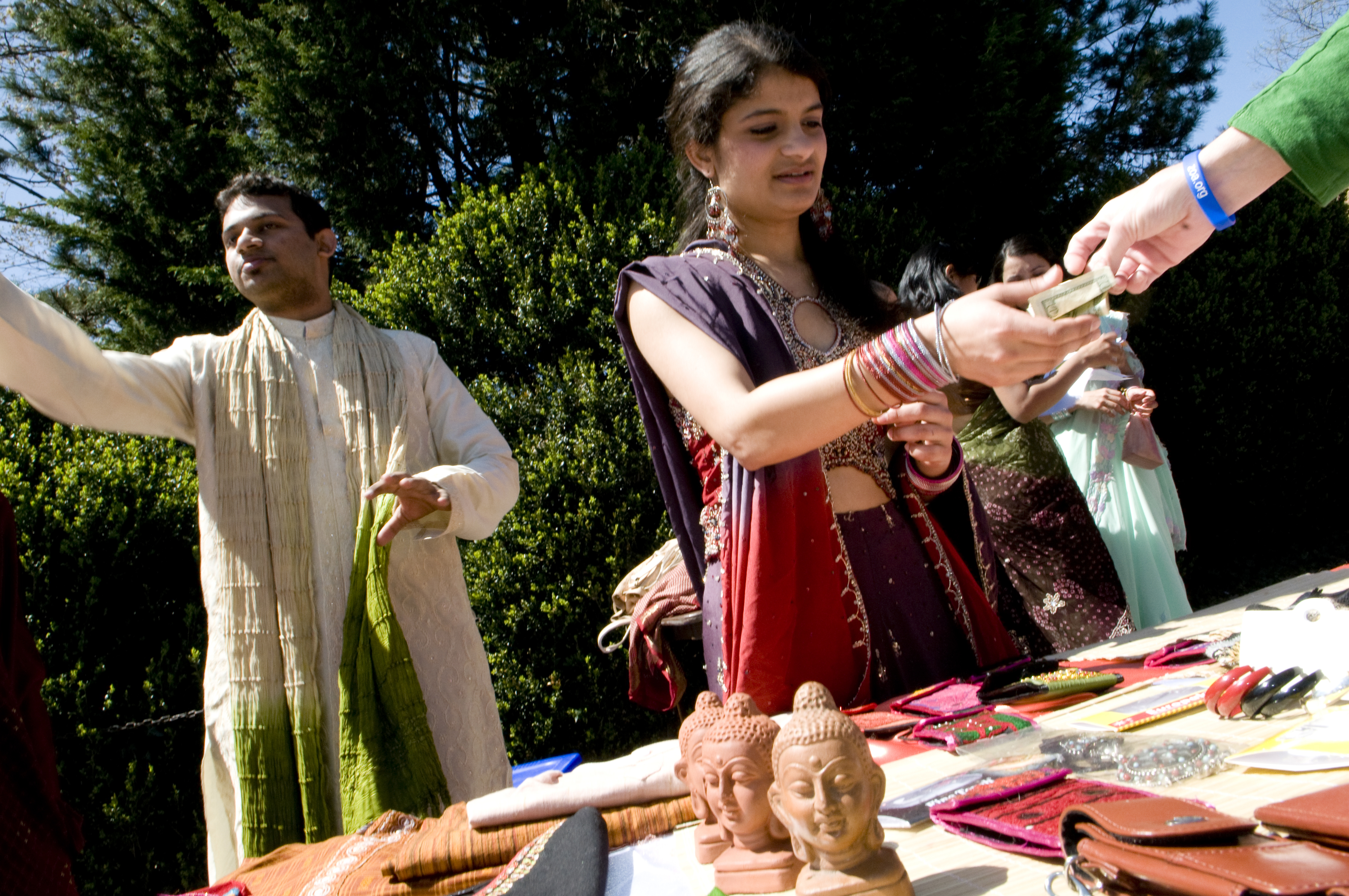 A young woman and young man stand behind a table at the street fair selling international crafts.