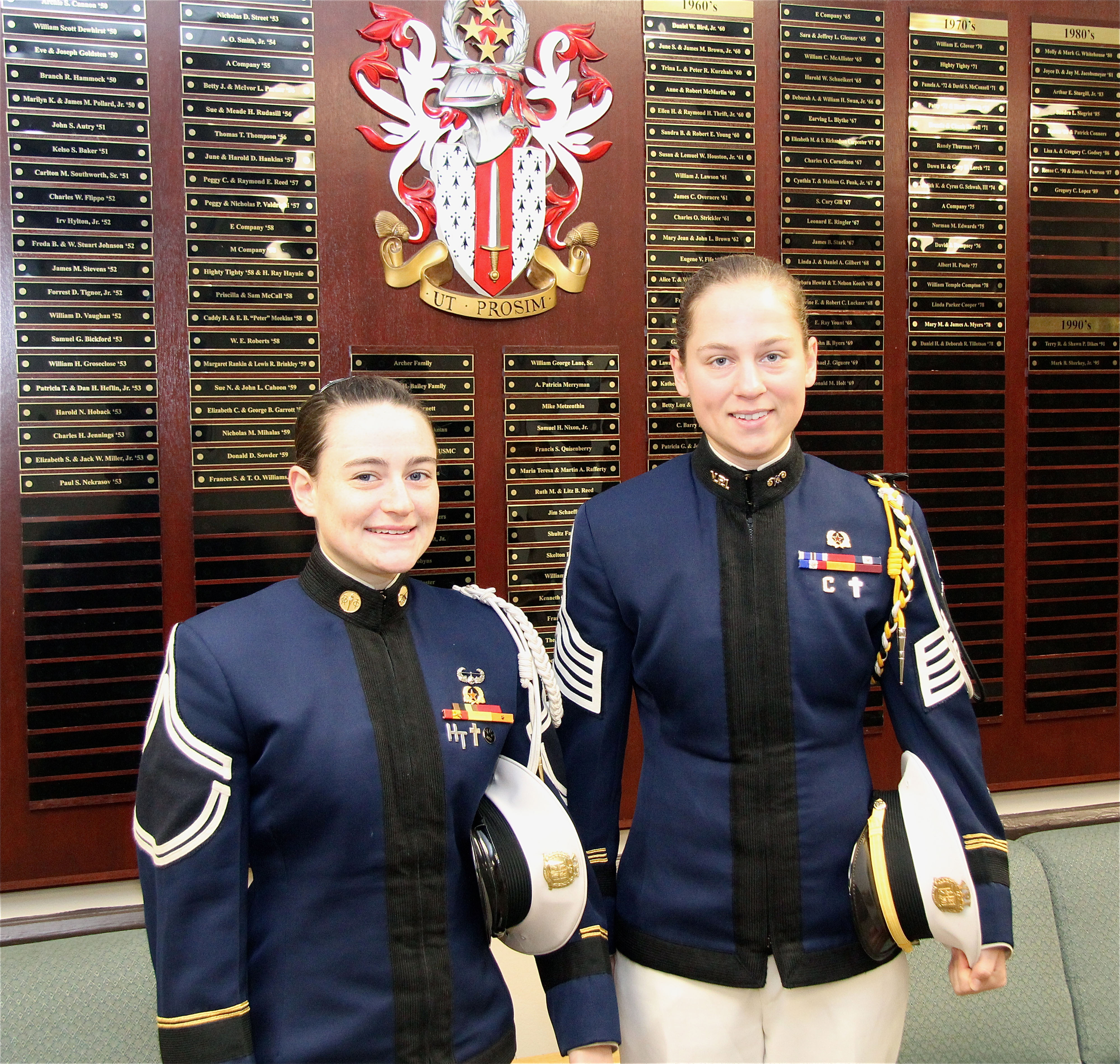 From left to right are Cadets Elaine Altman and Faith Mueller in front of the Corps of Cadets Donor Wall