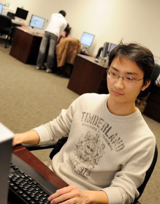 Graduate student at computer with other students in background.