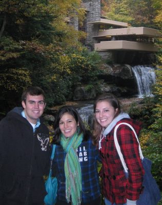 Three students stand in front of a house built over a waterfall. 