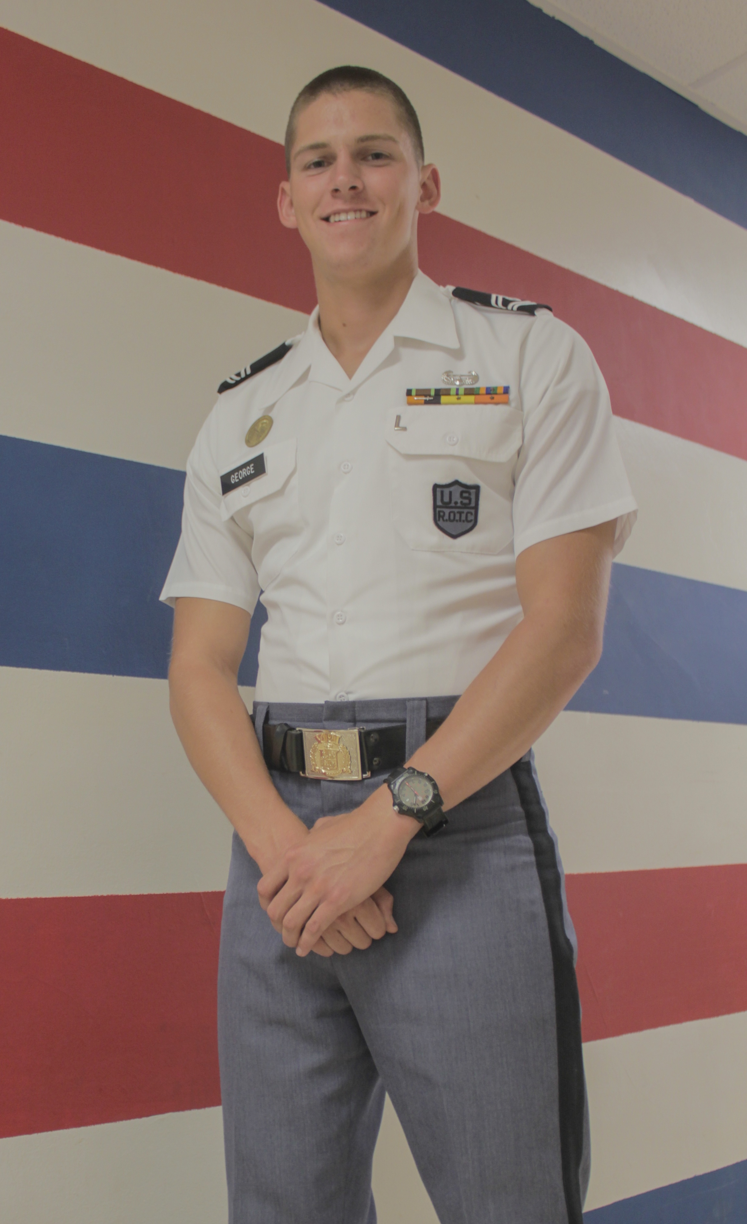 Cadet 1st Sgt. Andrew George stands in his company area against a wall painted with red, white, and blue stripes