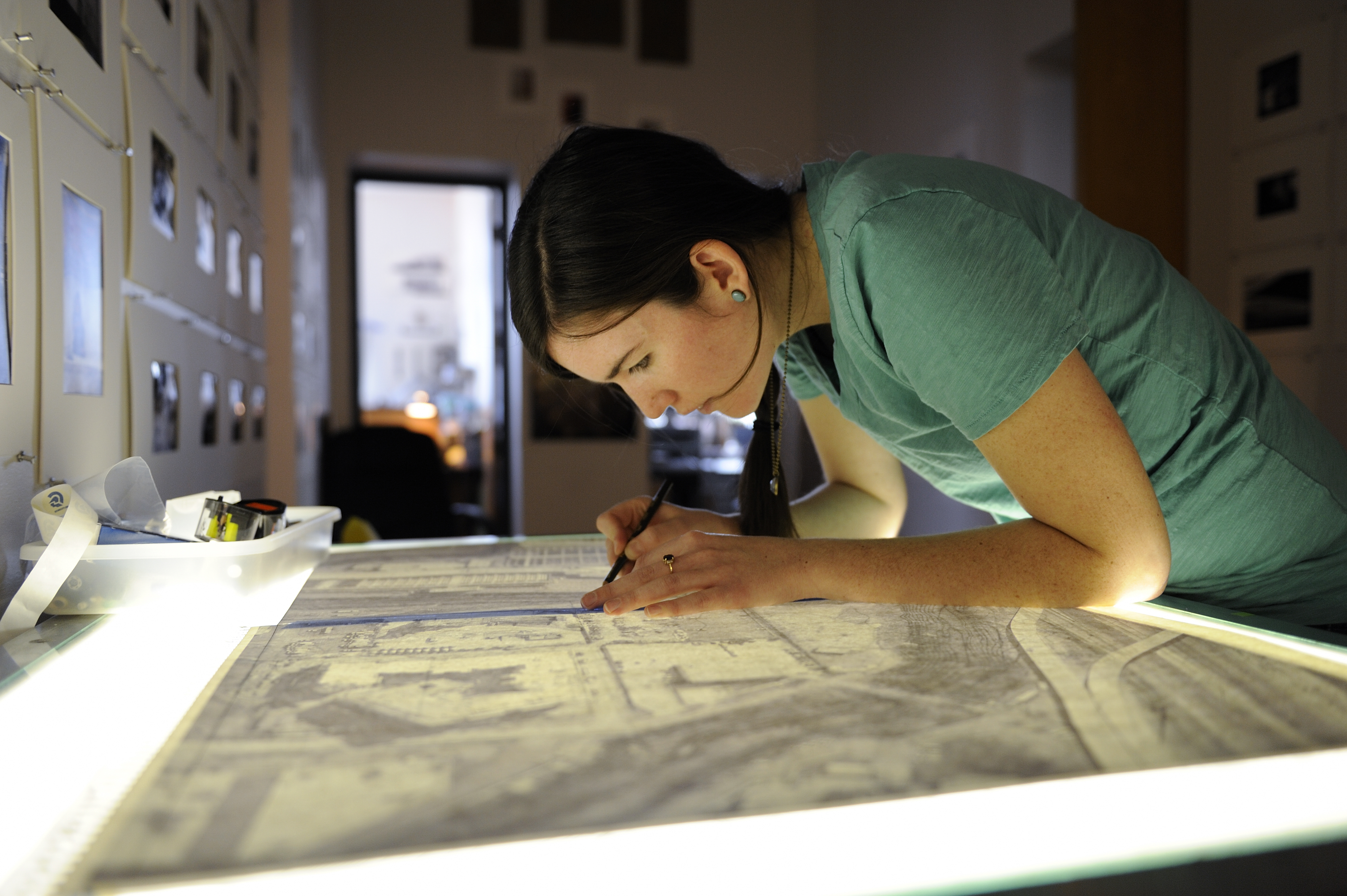 A girl bends over am architectural sketch on a light table.