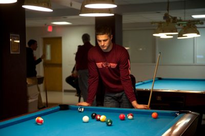 A student playing pool stares at the balls to figure out his next move. 