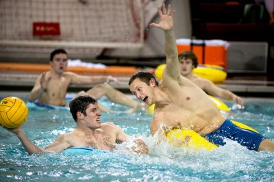 Two opponents battle it out in the pool playing inner-tube water polo. One tries to defend another throwing the ball to a teammate. 
