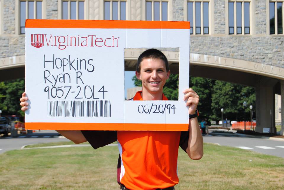 Ryan Hopkins holds a larger-than-life cardboard Hokie Passport on Virginia Tech's campus