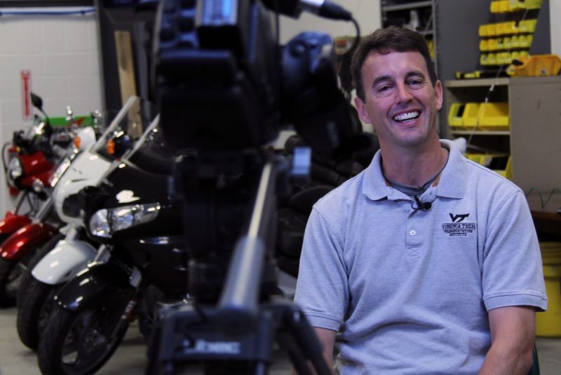 Shane McLaughlin, director of the Center for Automated Vehicle Systems at the transportation institute, sits next to motorcycles used for research.