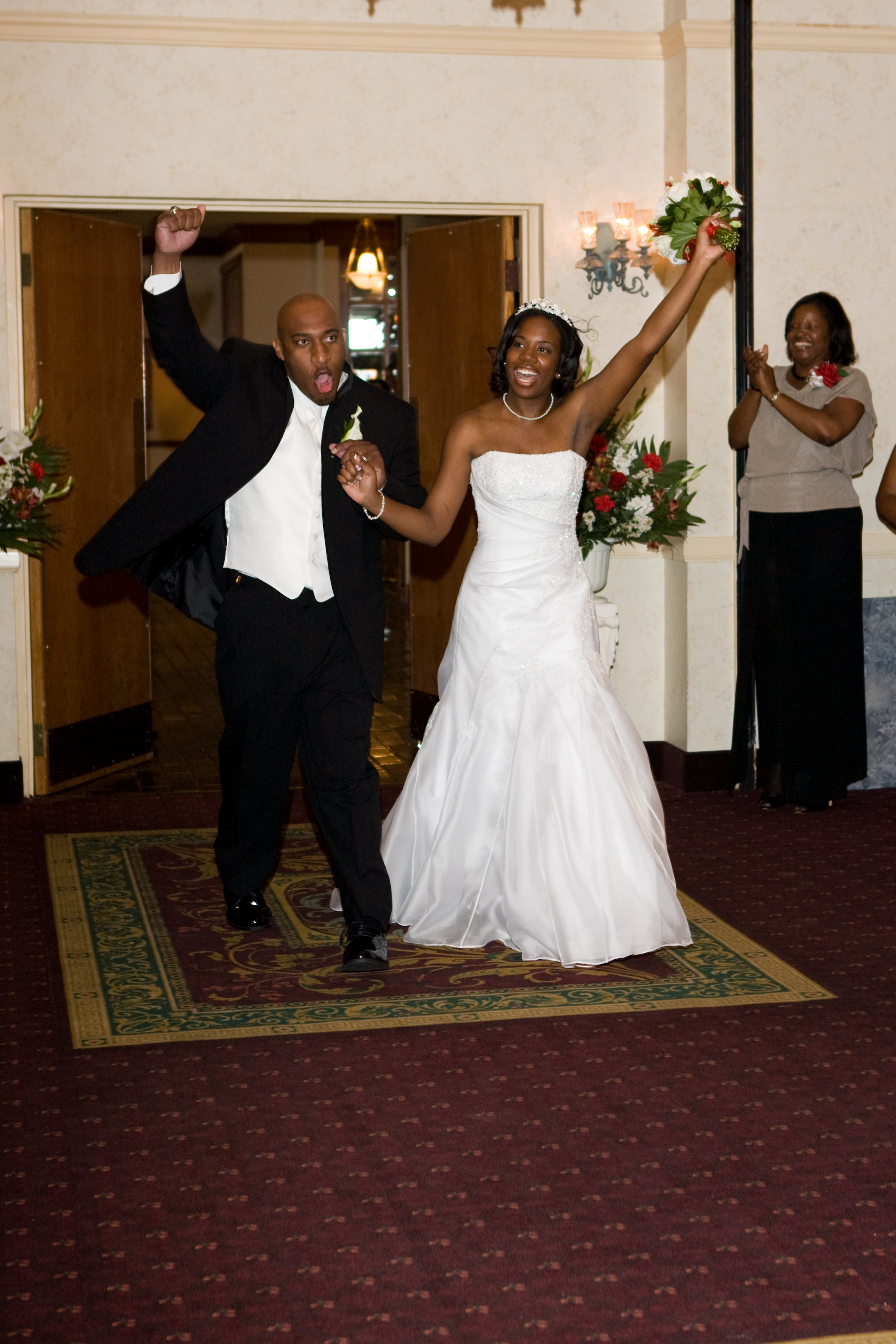 Image of the young couple walking into their reception holding hands and each raising an arm in a celebratory way.