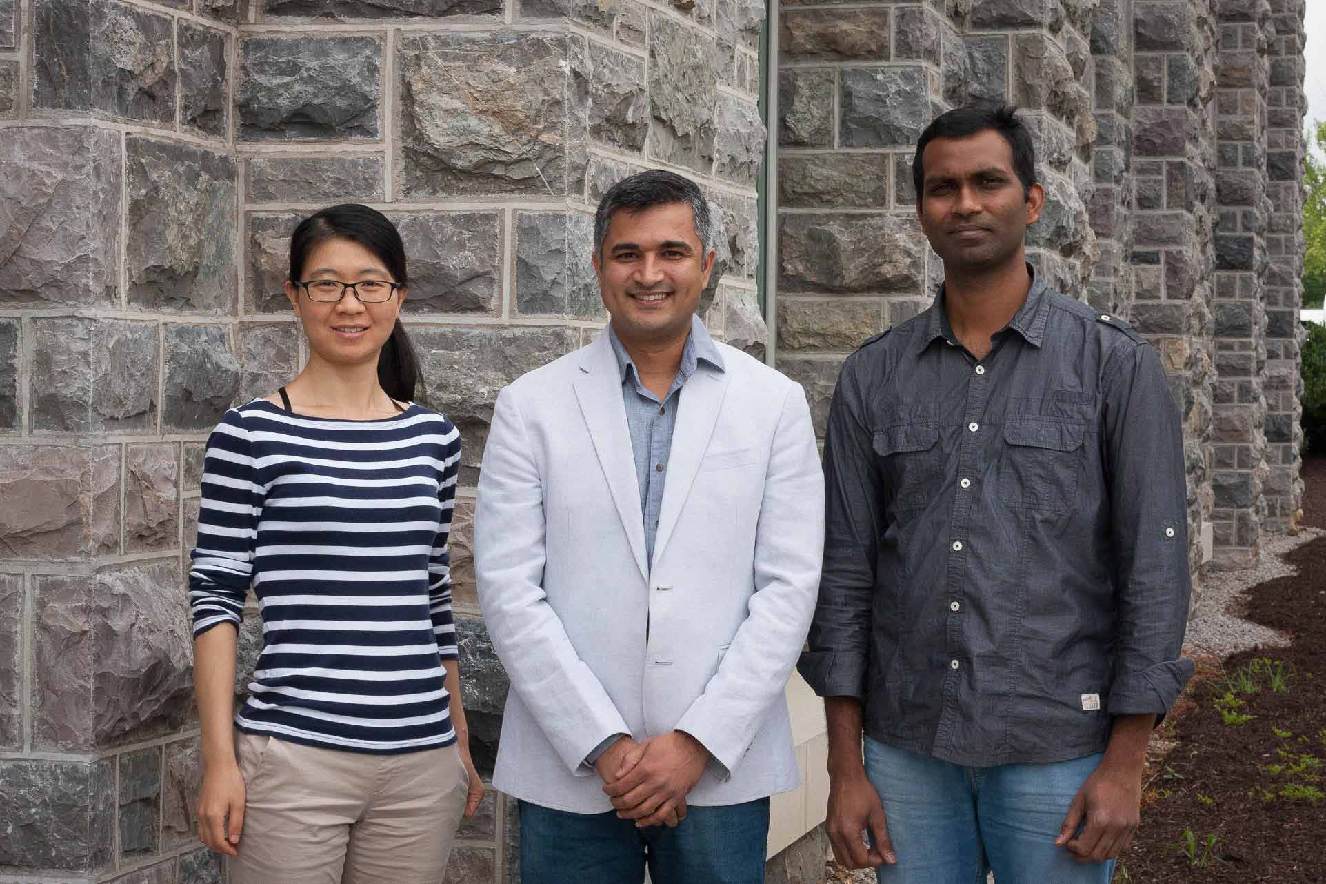 Three researchers pose for a photo in front of a Hokie stone backdrop.