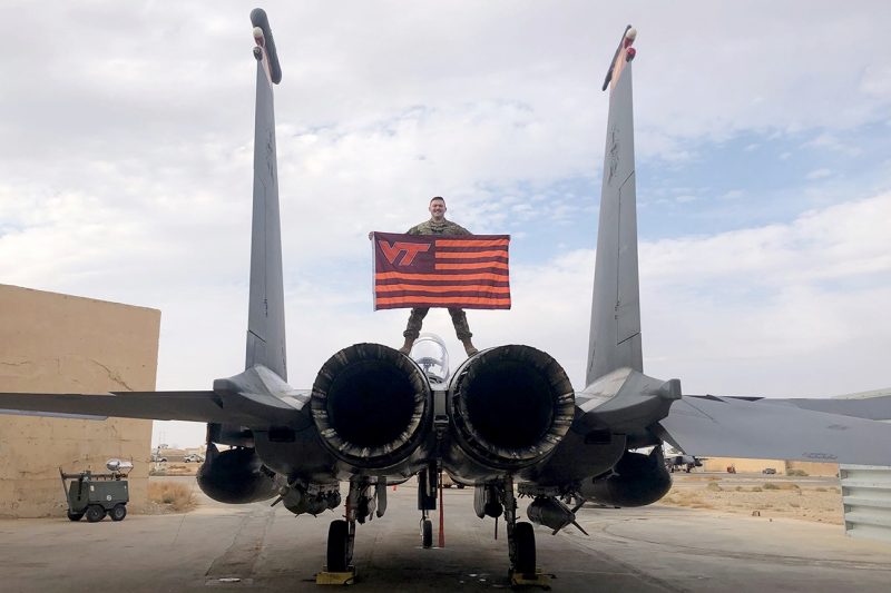 U.S. Air Force 1st Lt. Joshua Preiss holds a Virginia Tech flag while standing atop an aircraft.