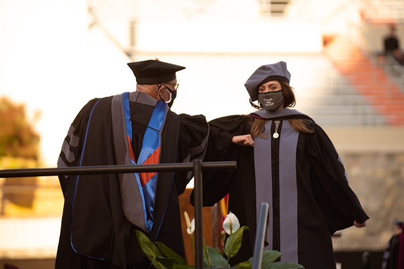 A newly hooded veterinary college graduate bumps elbows to celebrate