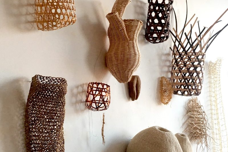 This detailed view of artist Ann Coddington's work "ephemera" shows this collection of baskets of different colors, shapes and sizes, hanging from a white wall.