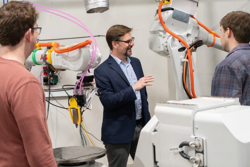 Three researchers gather around 3D printing robot.
