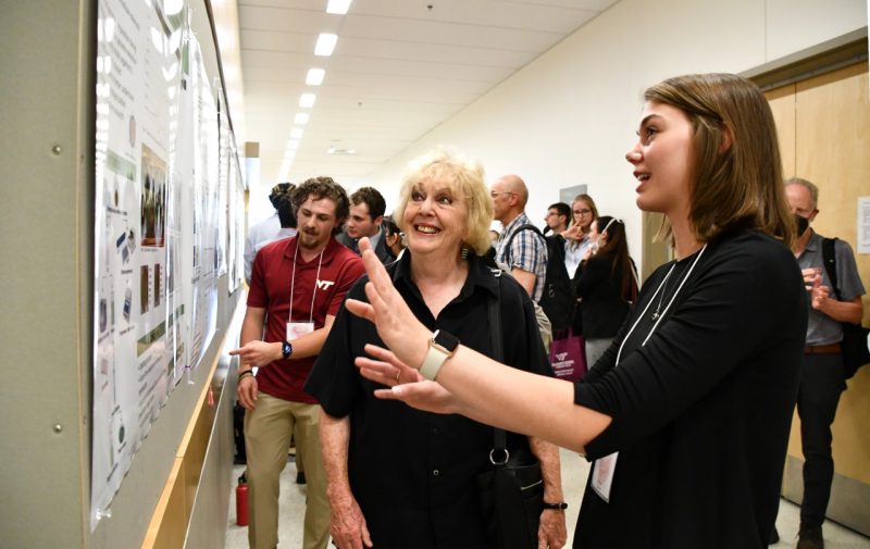 A young woman excitedly shows an older woman her research poster. 