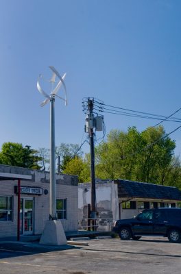 A verticle wind turbine in the forground with an electric pole in the near background