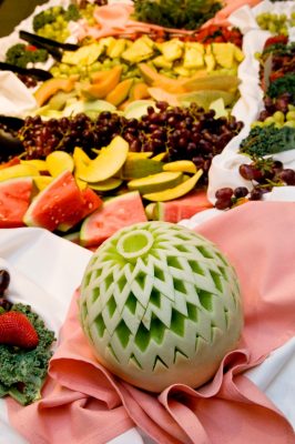 Display of variety of fruit and a hand-carved melon, foreground.