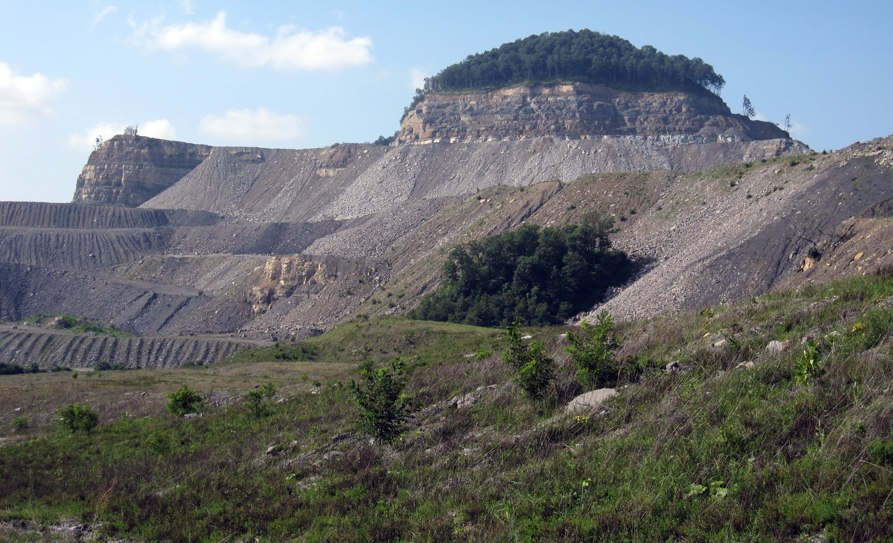 A mountaintop mining site, with a rocky outcrop topped with trees.