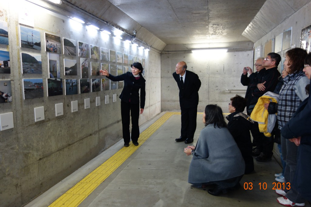 A group of Japanese people in a railway station looking at a photography exhibit on the wall. 