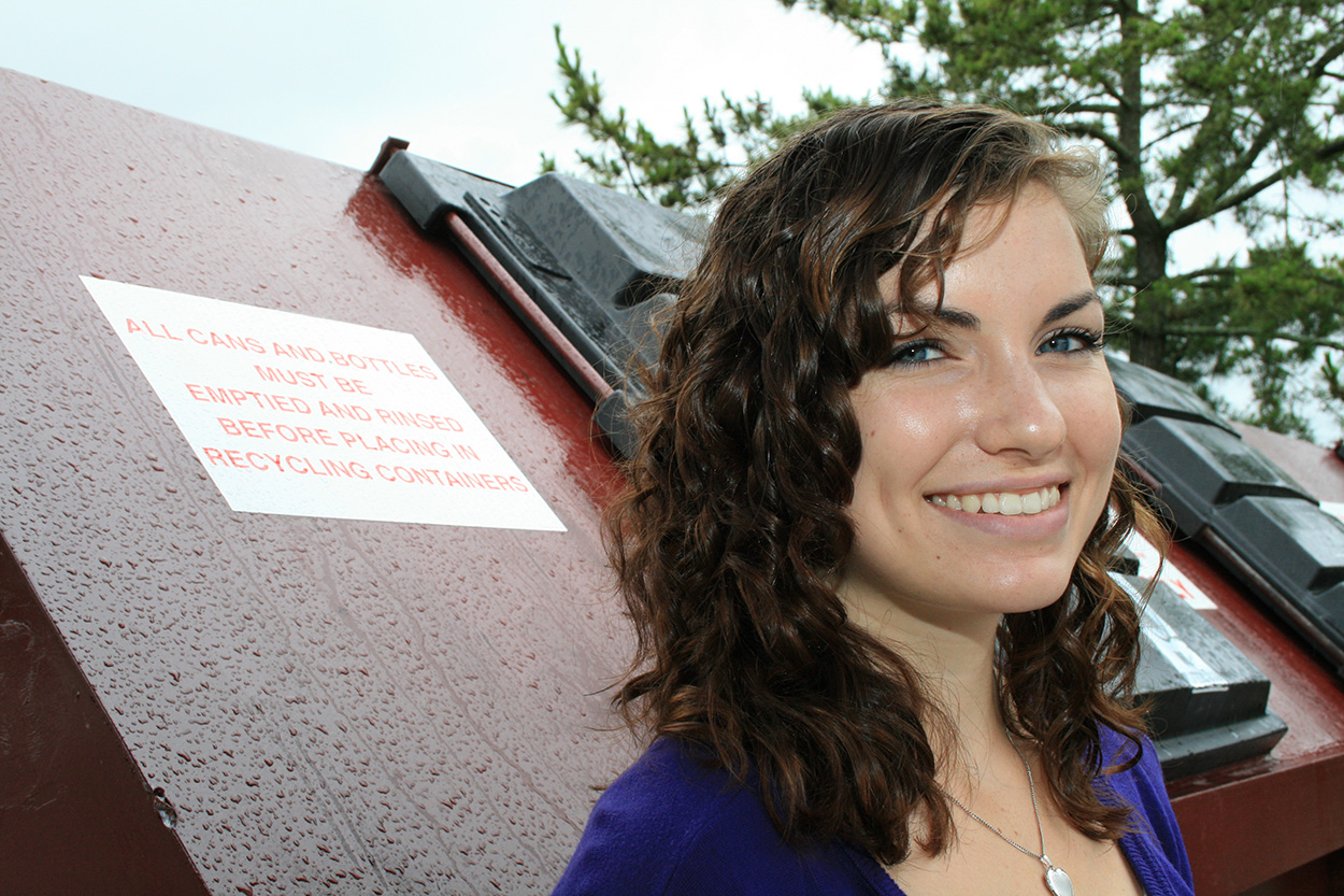 Lindsey Kummer stands in front of a dumpster.