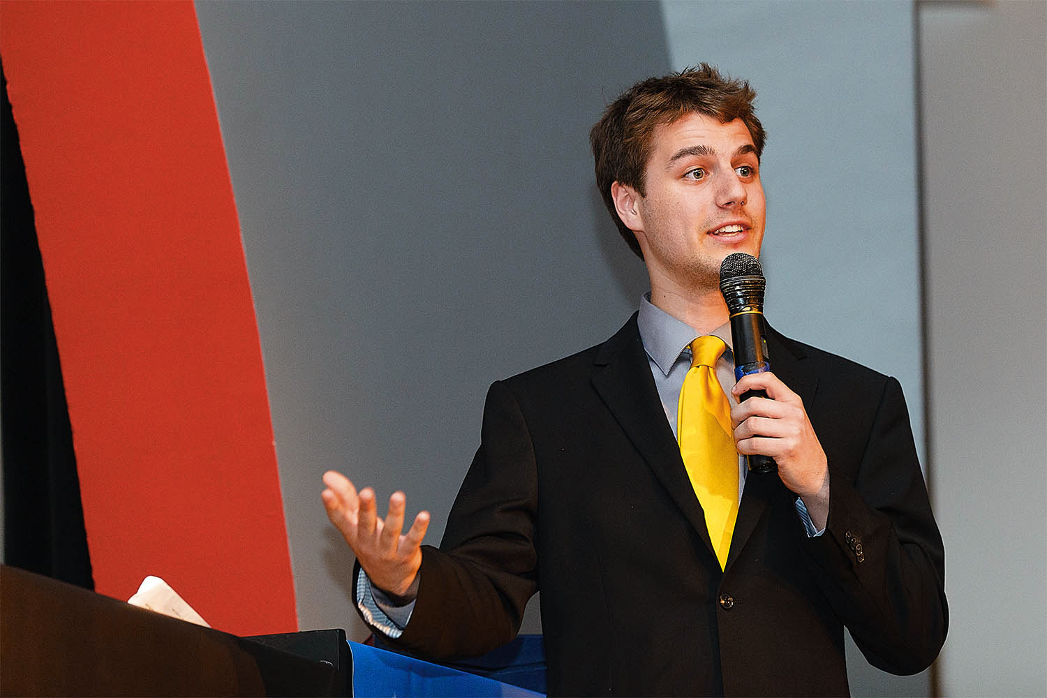 A young man on stage speaking into a microphone.