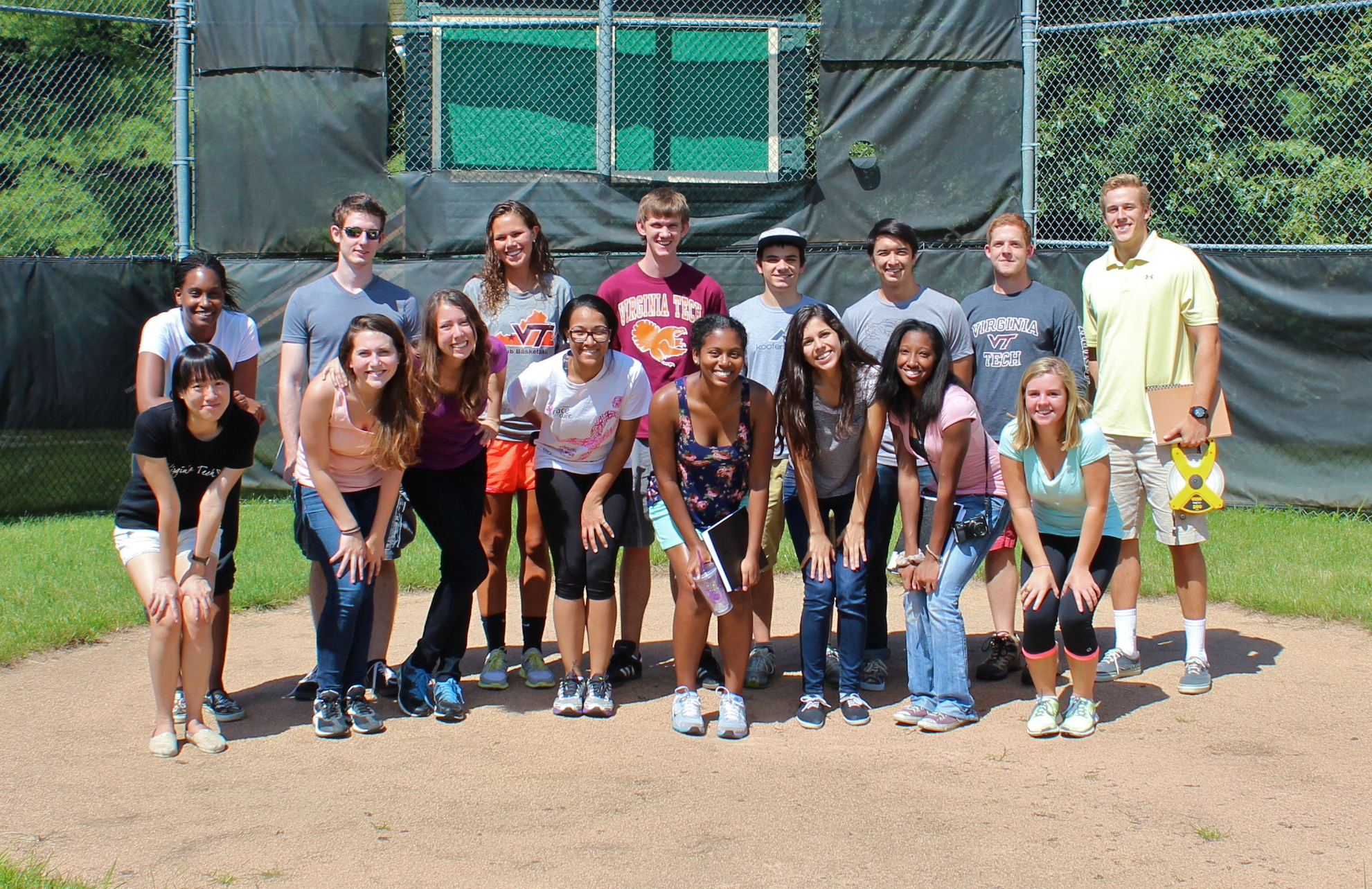 A group of 16 students stand on a baseball field.