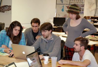 A team of five students gathers around a laptop working on their concept.
