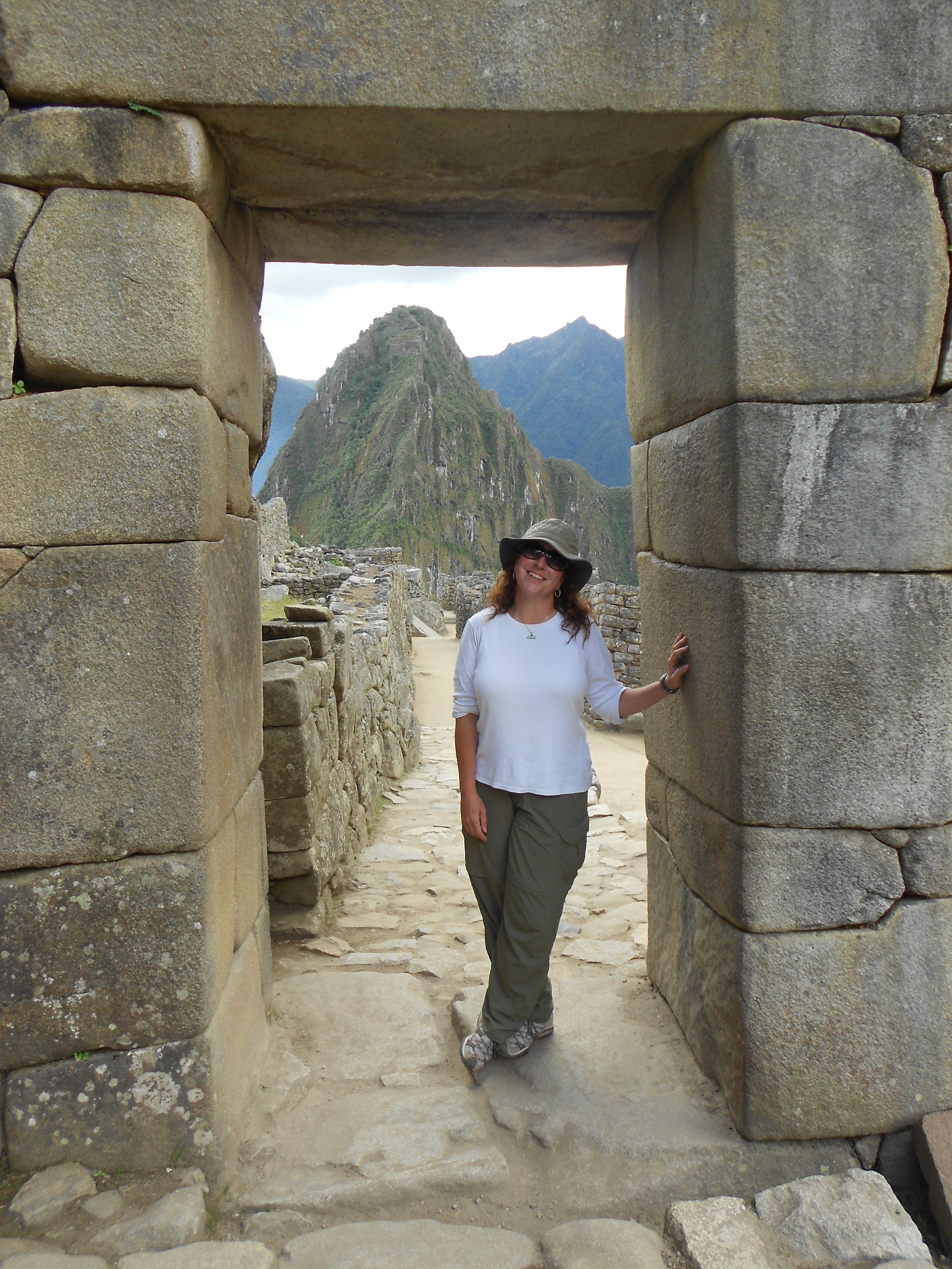 Christine Fiori stands in a stone doorway on a road leading towards the mountains at Machu Picchu.
