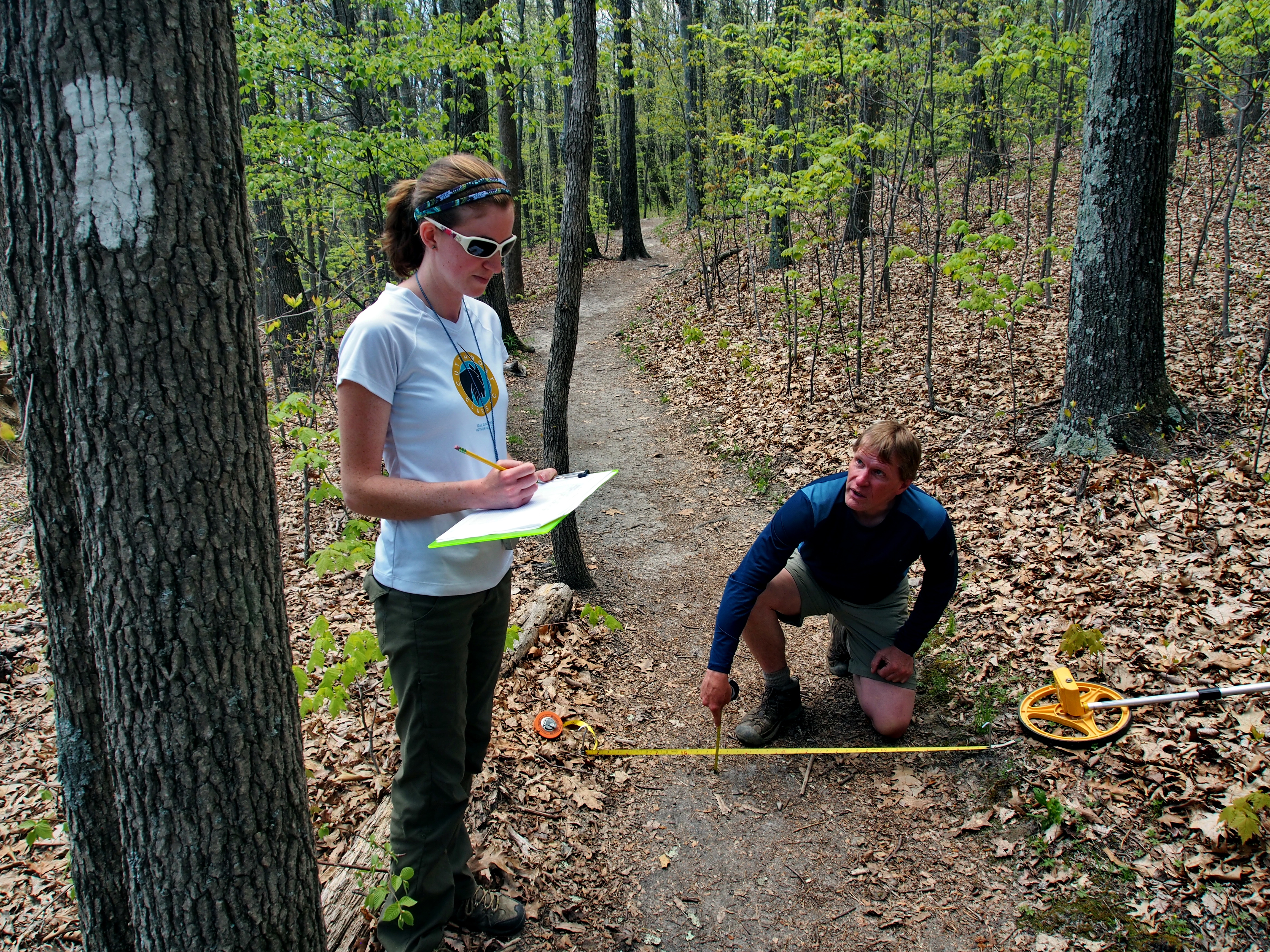 Two people measure a forest trail