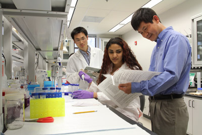 Hehuang Xie and two students at a laboratory bench look at samples. 
