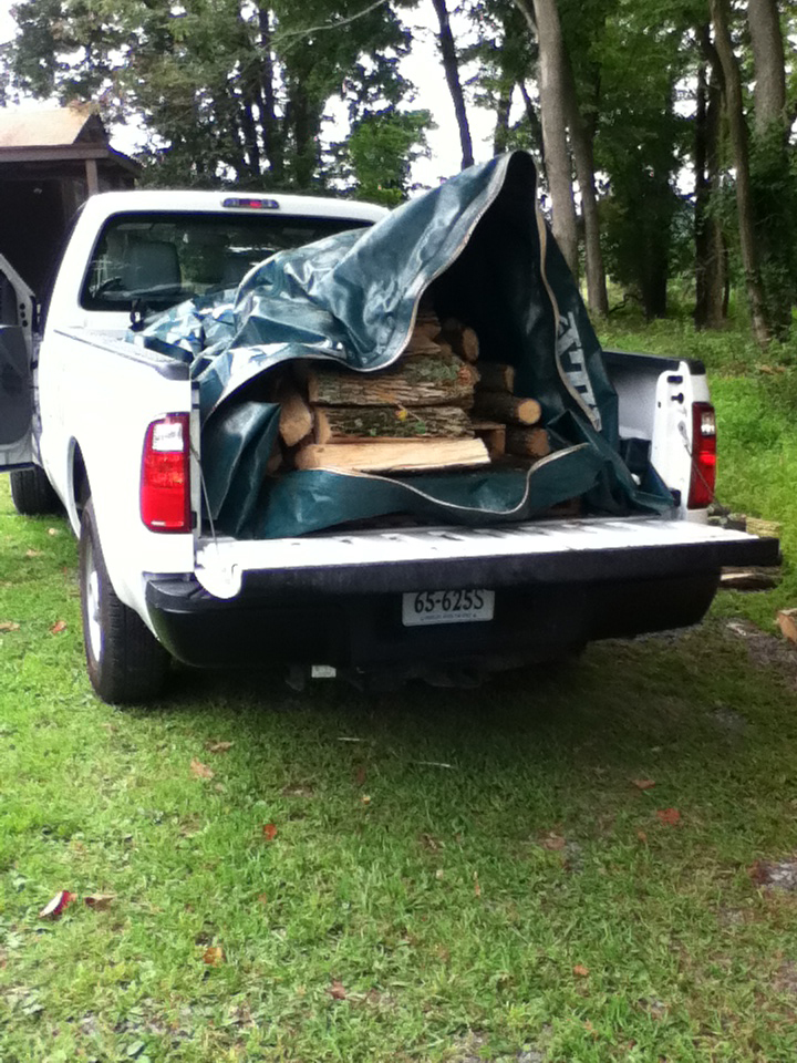 A load of firewood in large plastic bag in the bed of a pickup truck.