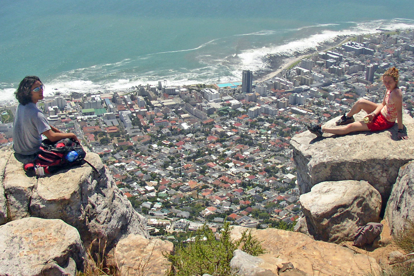 Two people sitting on a mountaintop above a city.