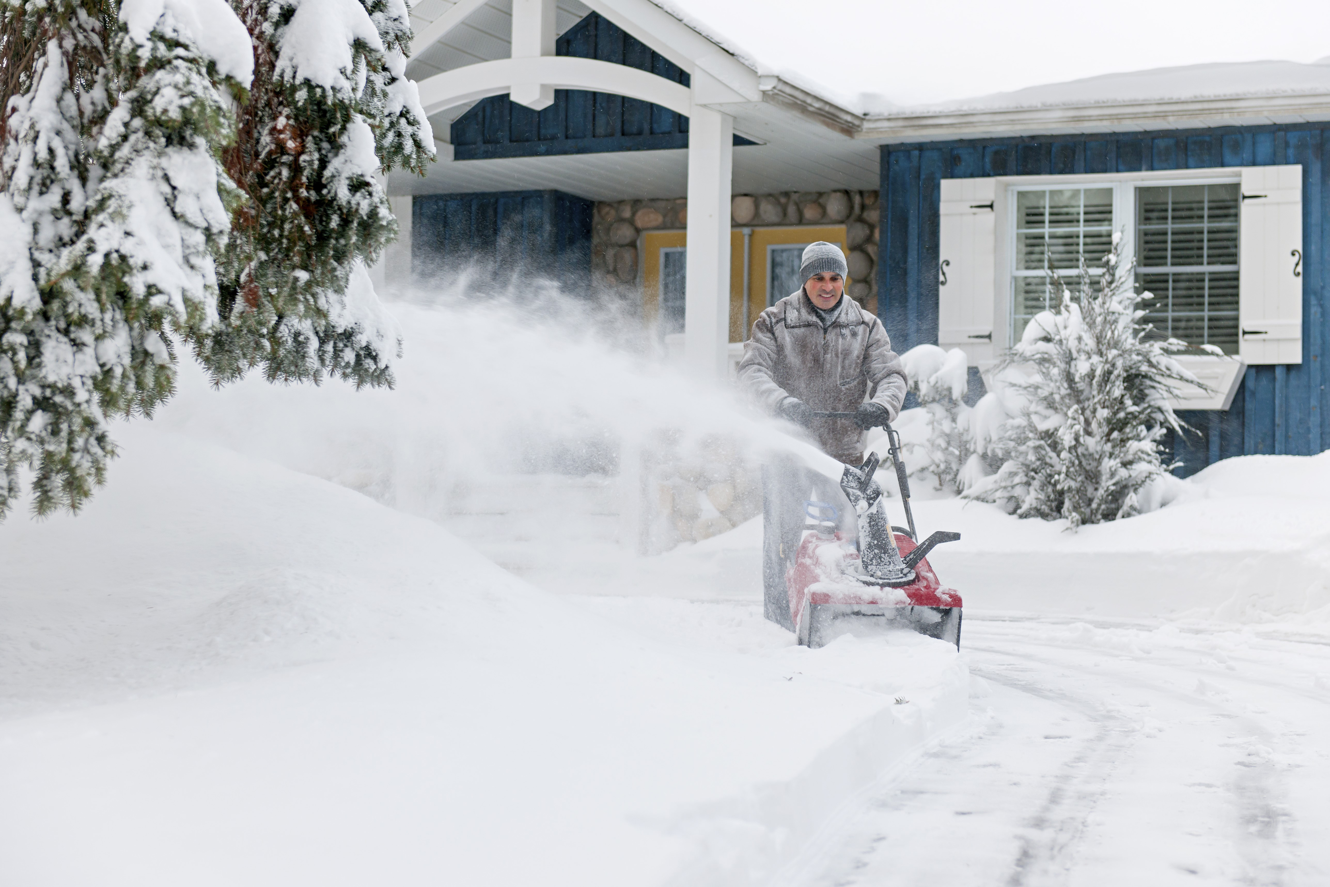 white male operating a snow blower in front of a blue house