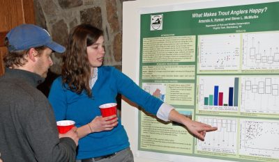 Amanda Hyman points to a poster while a meeting attendee looks on.
