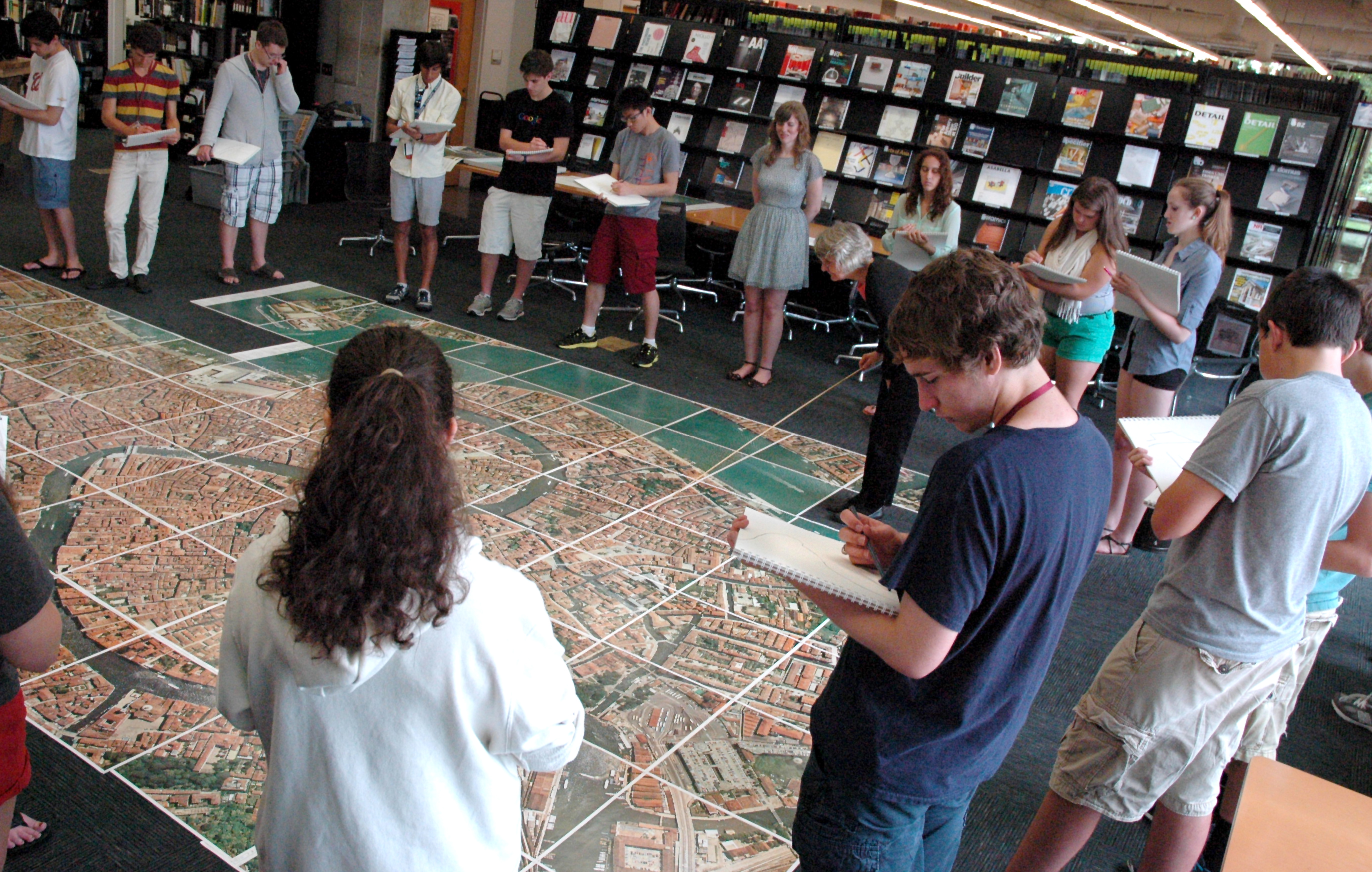 Students with sketchbooks gather around a large map on the floor.