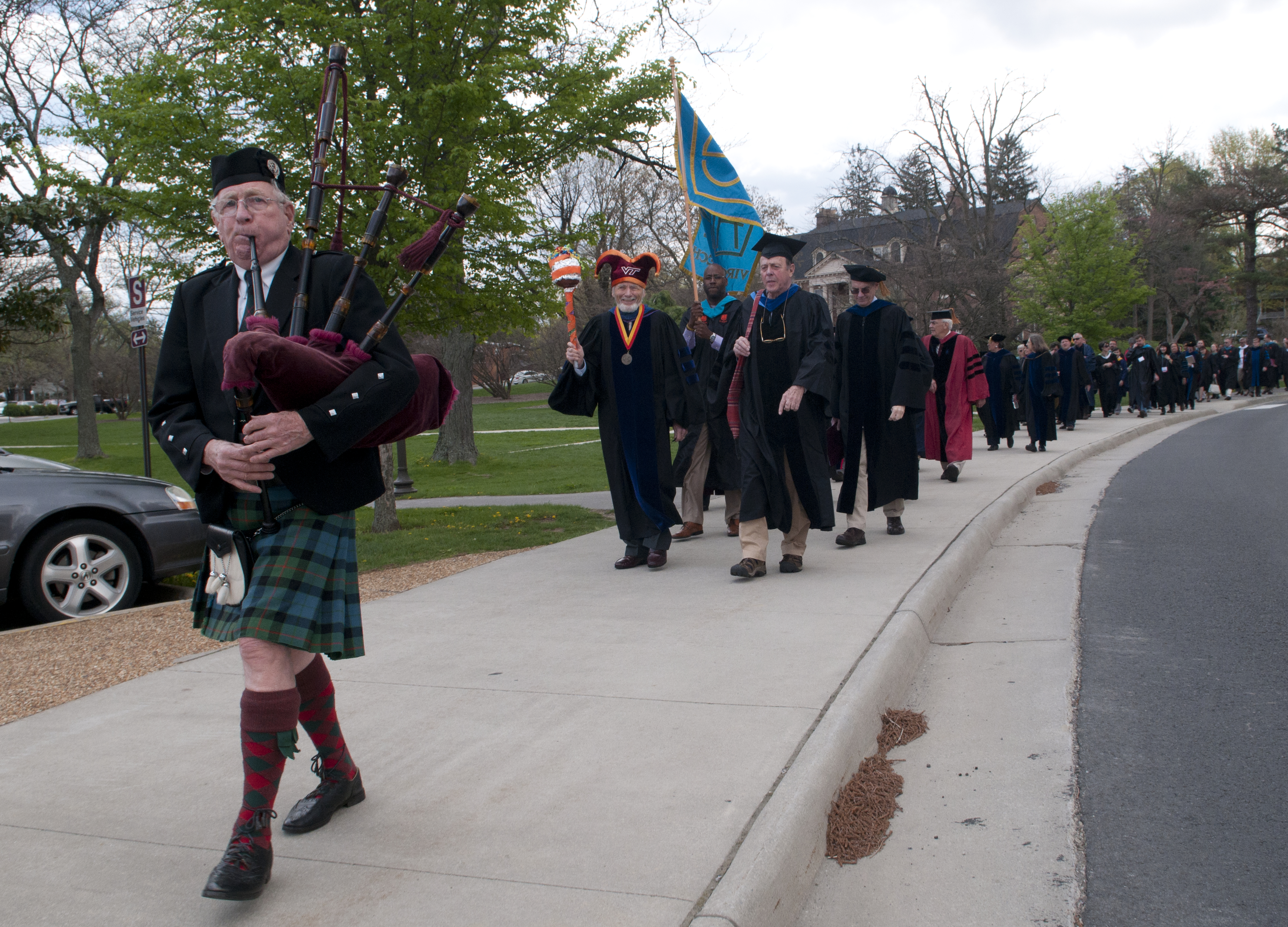 A bagpiper leads a procession of faculty in full academic regalia. 
