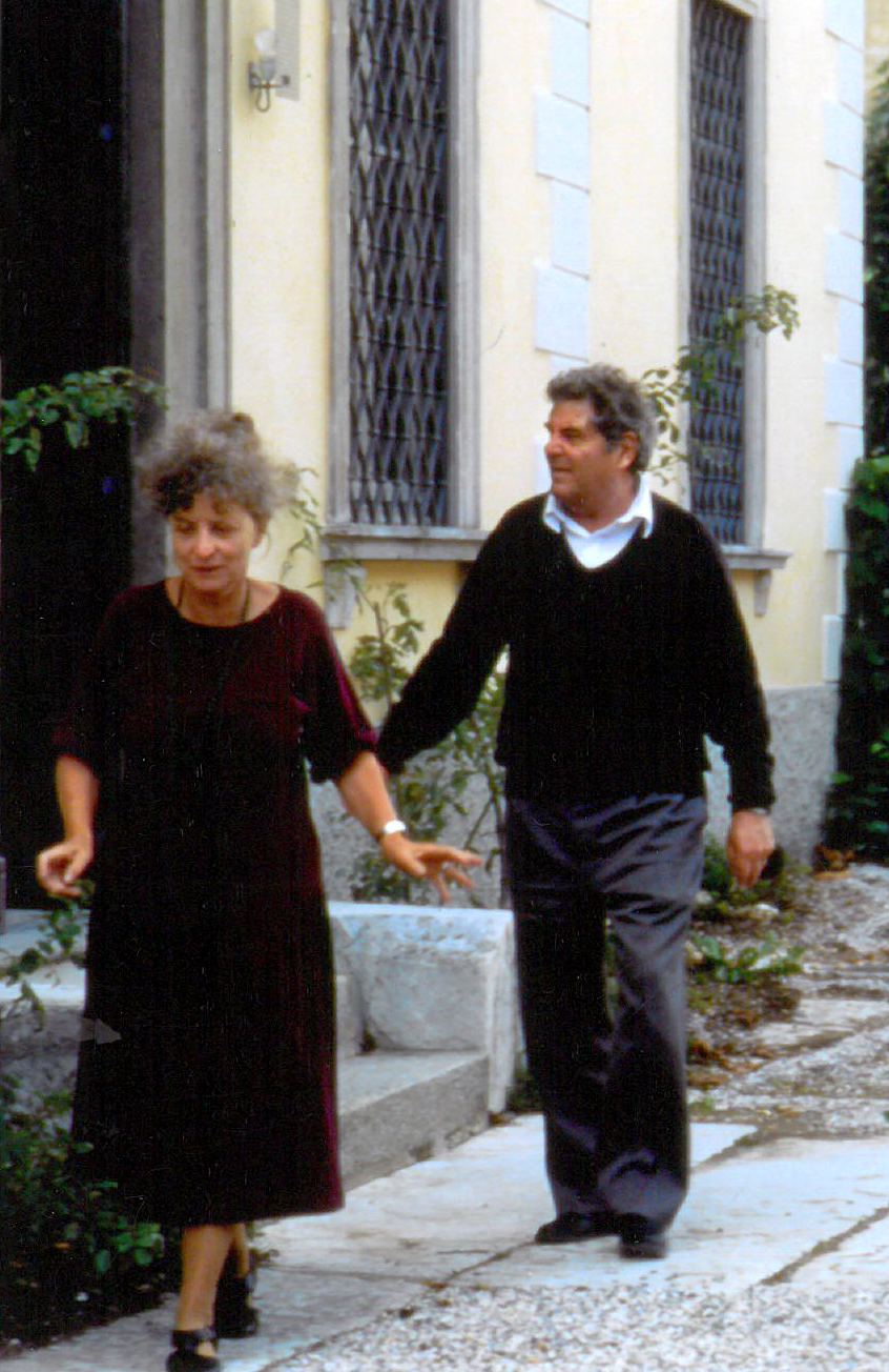 Lucy and Olivio Ferrari walk along the sidewalk in front of the large yellow villa. 