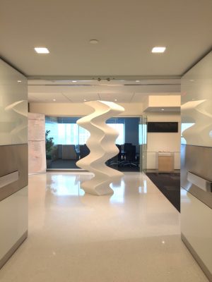 A six-foot white undulating column on display in the hallway of an office building. 
