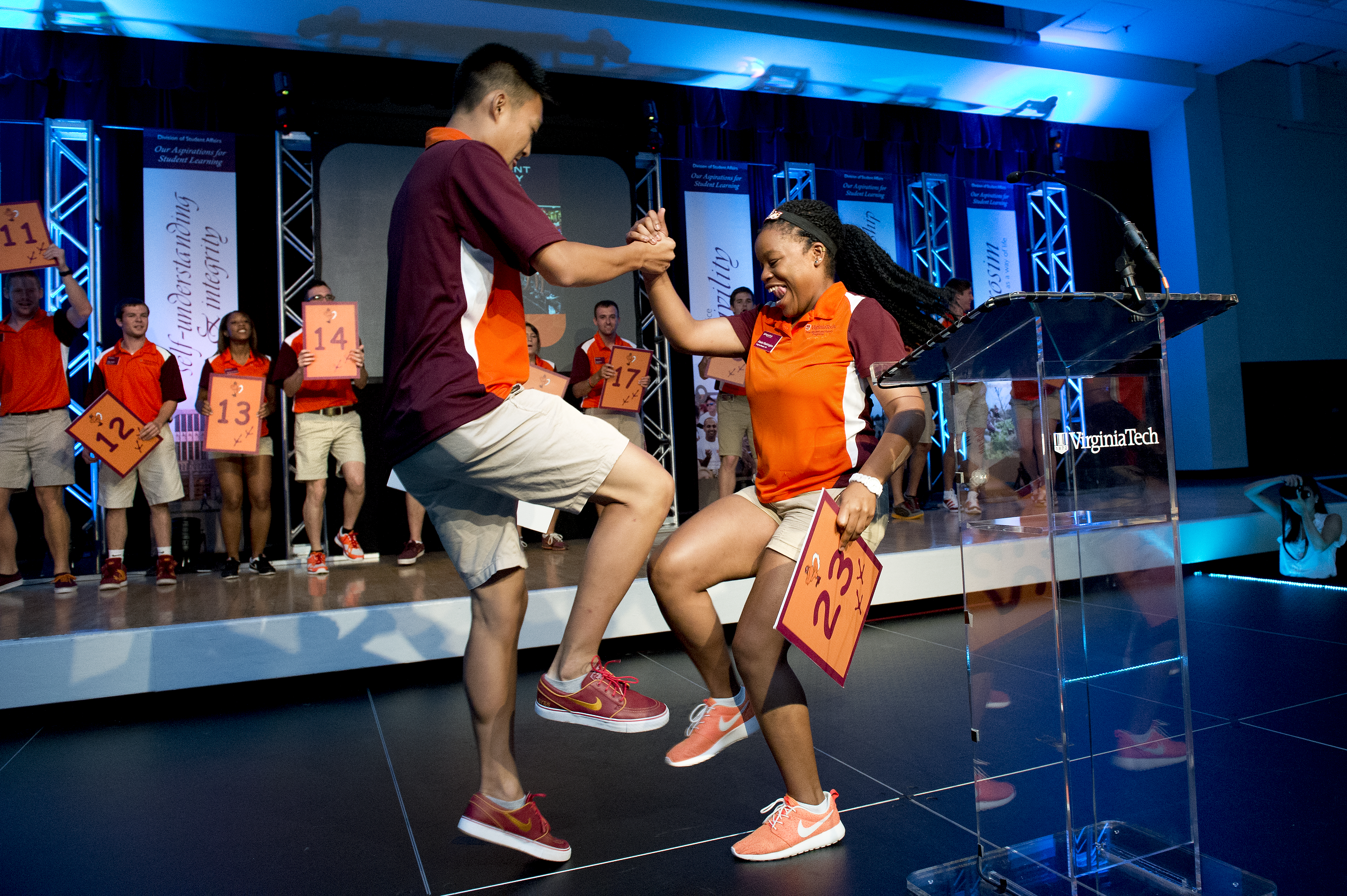Two Orientation staff members do a handshake on stage at the opening session of Orientation.