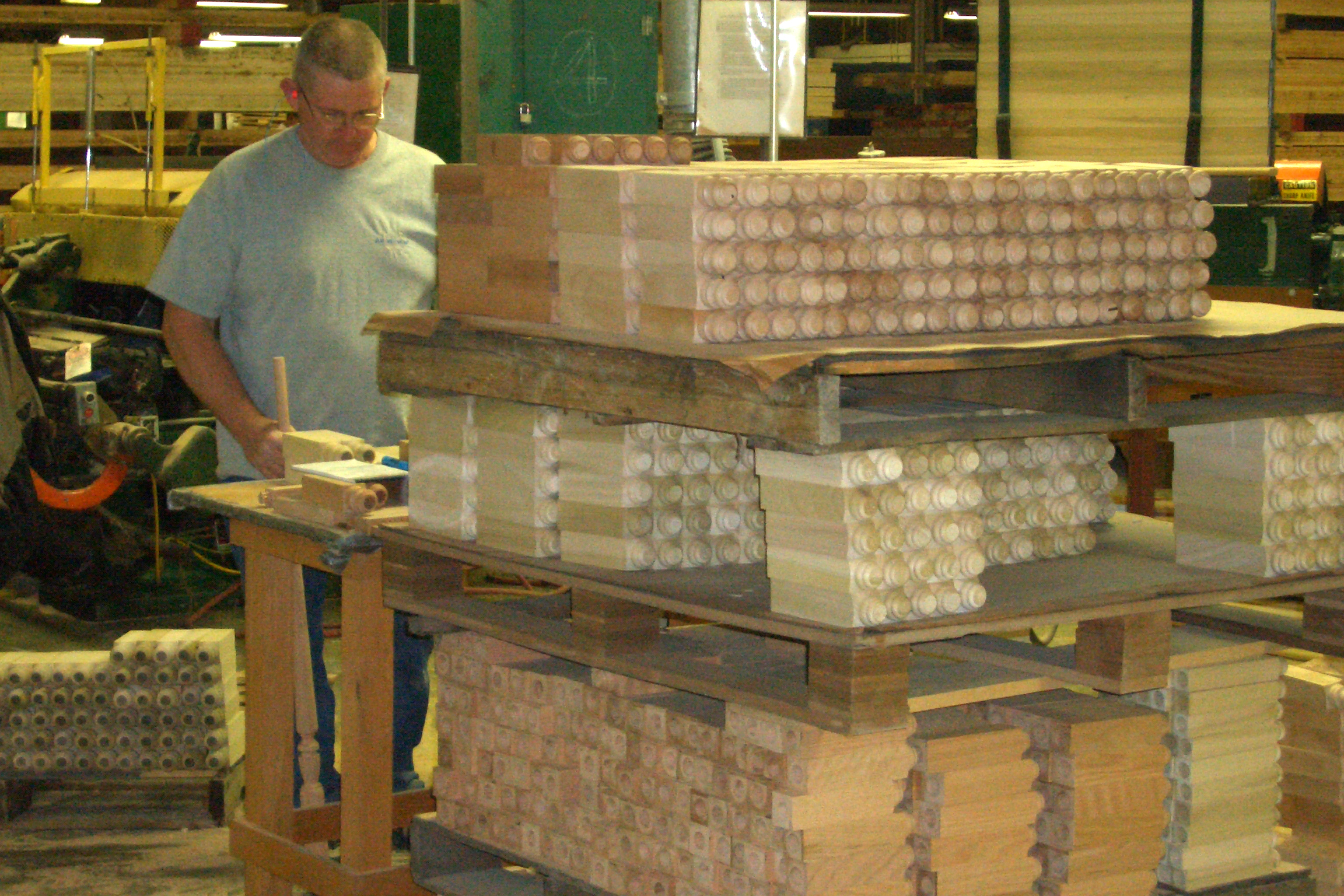 A man stands behind a pallet of wooden stair parts in a factory.