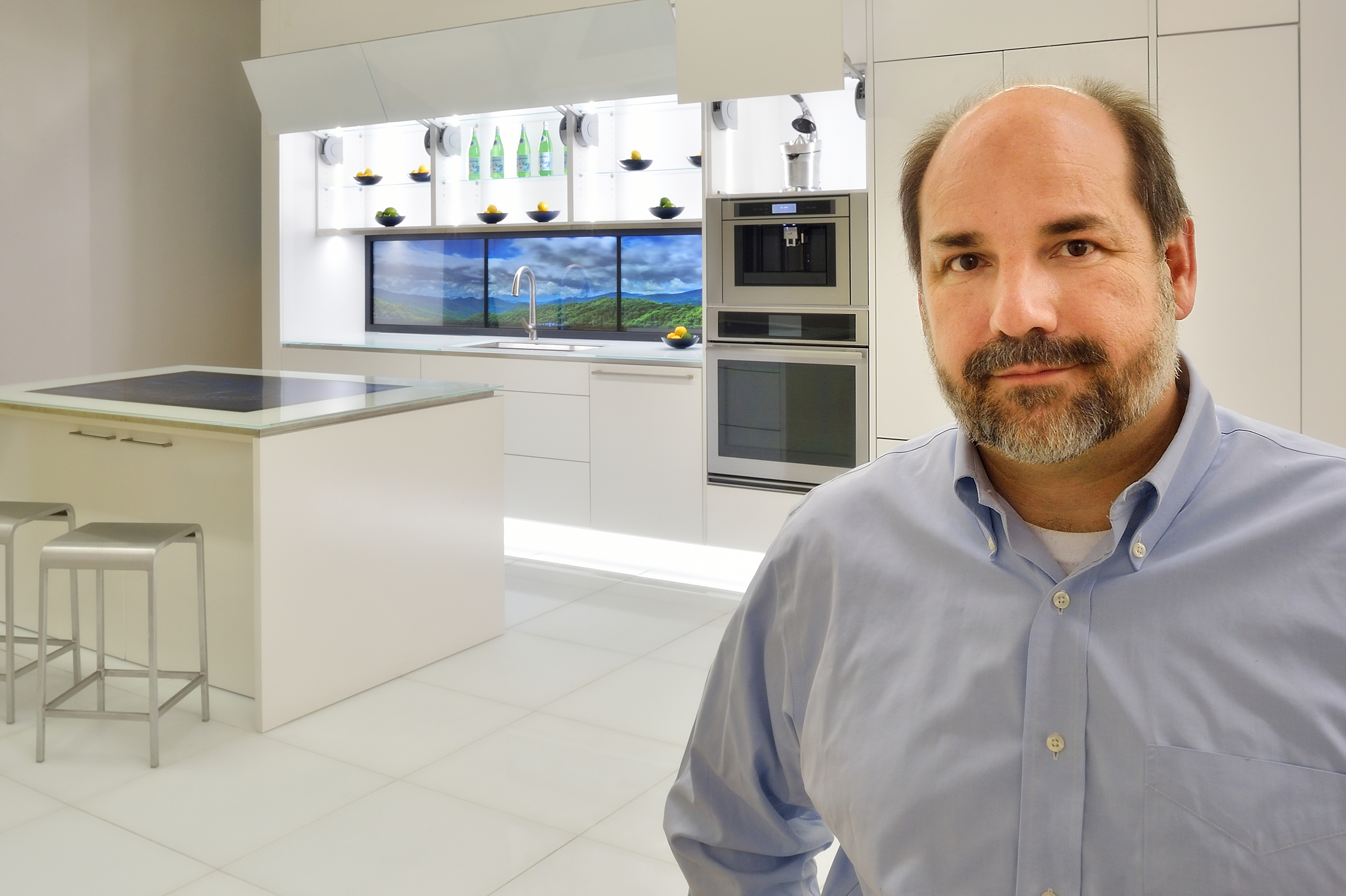 Joseph Wheeler stands in the foreground with a bright white kitchen with lighted cabinets in the background.