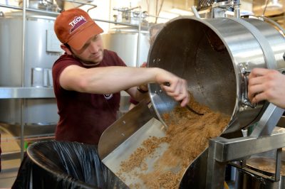 A student spoons out spent barley from the brewhouse container into a trashcan. The professional-grade brewhouse is similar to what most craft beermaking facilities use, but optimized for teaching.