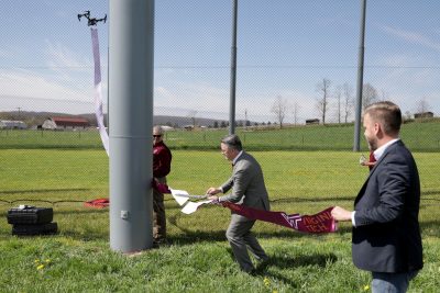 Flanked by UAS Safety Manager Greg Calvert (at left) and Mark Blanks, the director of the Virginia Tech Mid-Atlantic Partnership, President Sands cut a ribbon held aloft by a drone. 