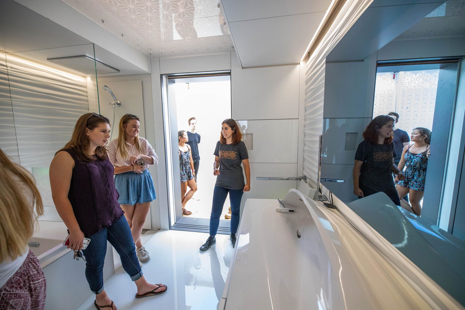 Three women stand inside a futuristic-looking bathroom, complete with a 3D printed sink.