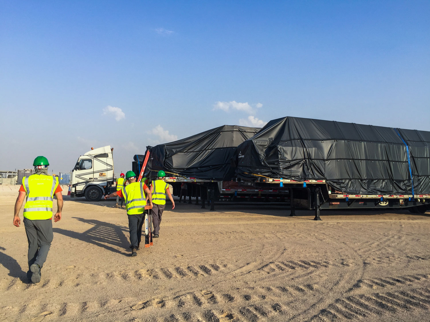 A photo in the desert of workers heading toward a truck loaded with a house covered by black tarps.