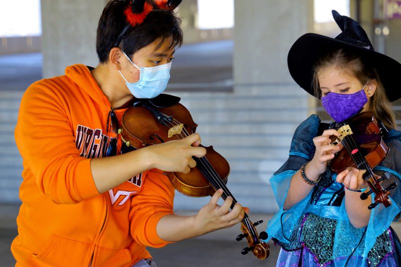 James Kim, a first-year music education student, instructs a Montgomery County student. They both donned Halloween costumes for a special Virginia Tech String Project gathering in the Perry Street Parking Garage.