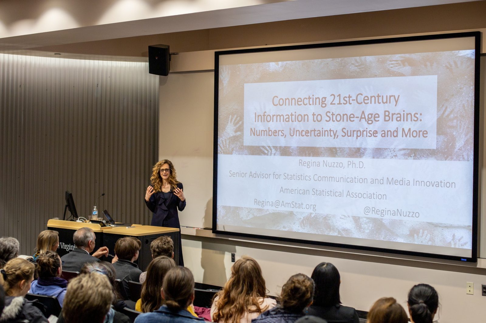 Regina Nuzzo kicked off the two-day event with an inspirational keynote address. A woman with large curly blonde hair is standing in front of a crowd, with a large projection screen behind her. Photo courtesy of Alex Freeze.
