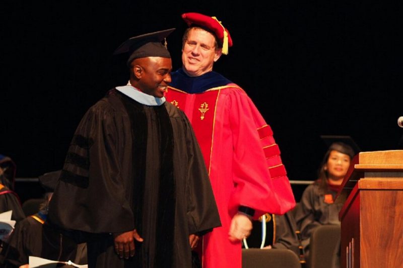 William “Bill” Glenn (center) hoods a graduate student during Commencement.