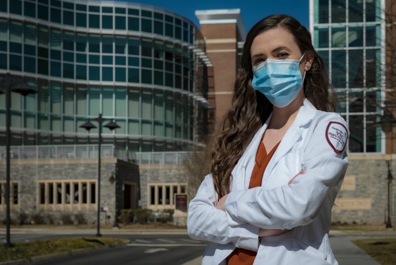 Woman wearing mask and white medical coat standing in front of building