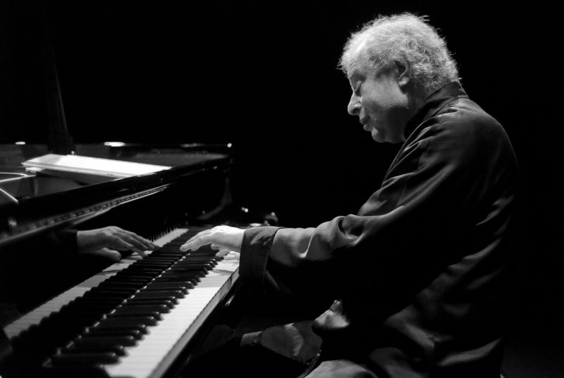 This black and white photo shows Andras Schiff at the piano getting ready to touch the keys with his left hand.