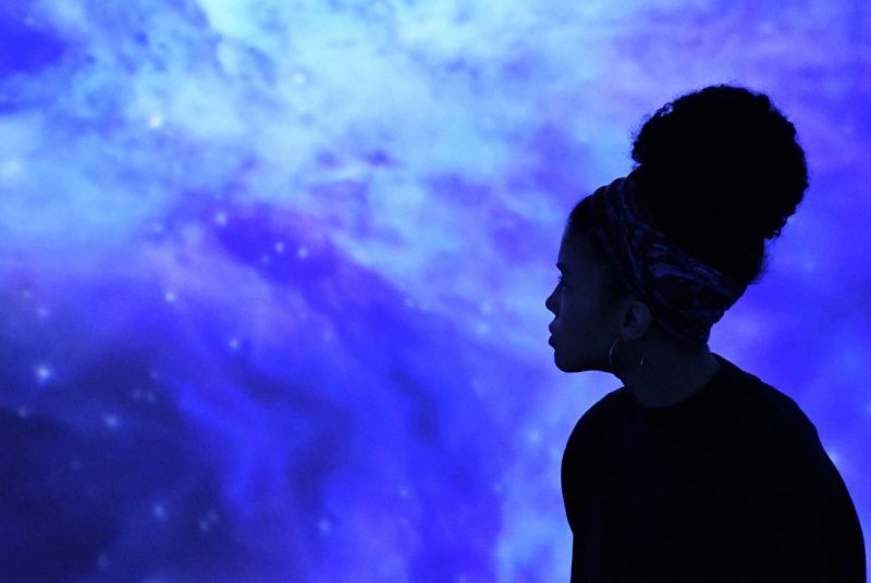 A silhouette of student Hayley Oliver poses in front of a rich, dark blue image of space projected on a screen.